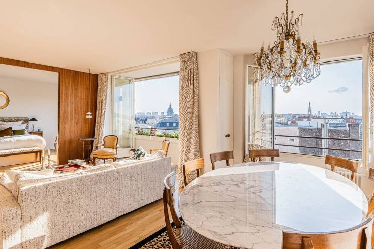 Intérieur d'un appartement du 7e arrondissement de Paris, avec un salon lumineux et une salle à manger autour d'une table en marbre, offrant une vue sur la ville.
