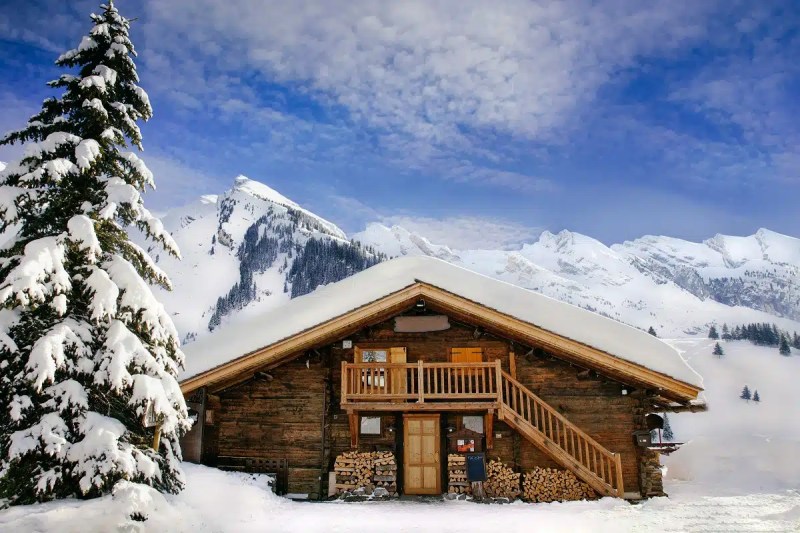 Chalet en bois traditionnel sous la neige, avec un balcon en bois et un environnement montagneux majestueux.