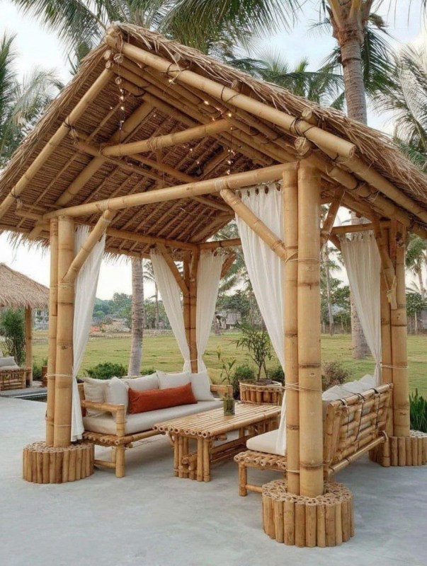 Bamboo gazebo with comfortable seating and decorative curtains in a tropical setting.